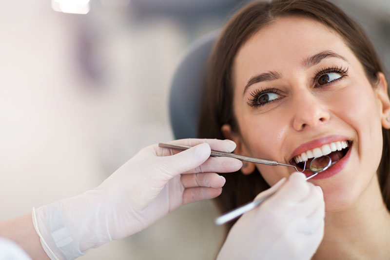 a woman smiling with a dentist holding tools to her mouth to clean it