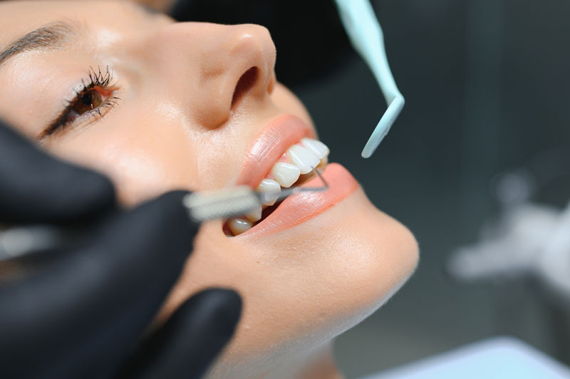 Doctor examining patient's teeth, closeup. Black gloves with dental tool in hand, up-close image of dental examination.