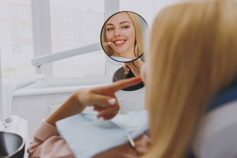 Young smiling satisfied fun happy calm woman 20s reflected in mirror sitting at dental office