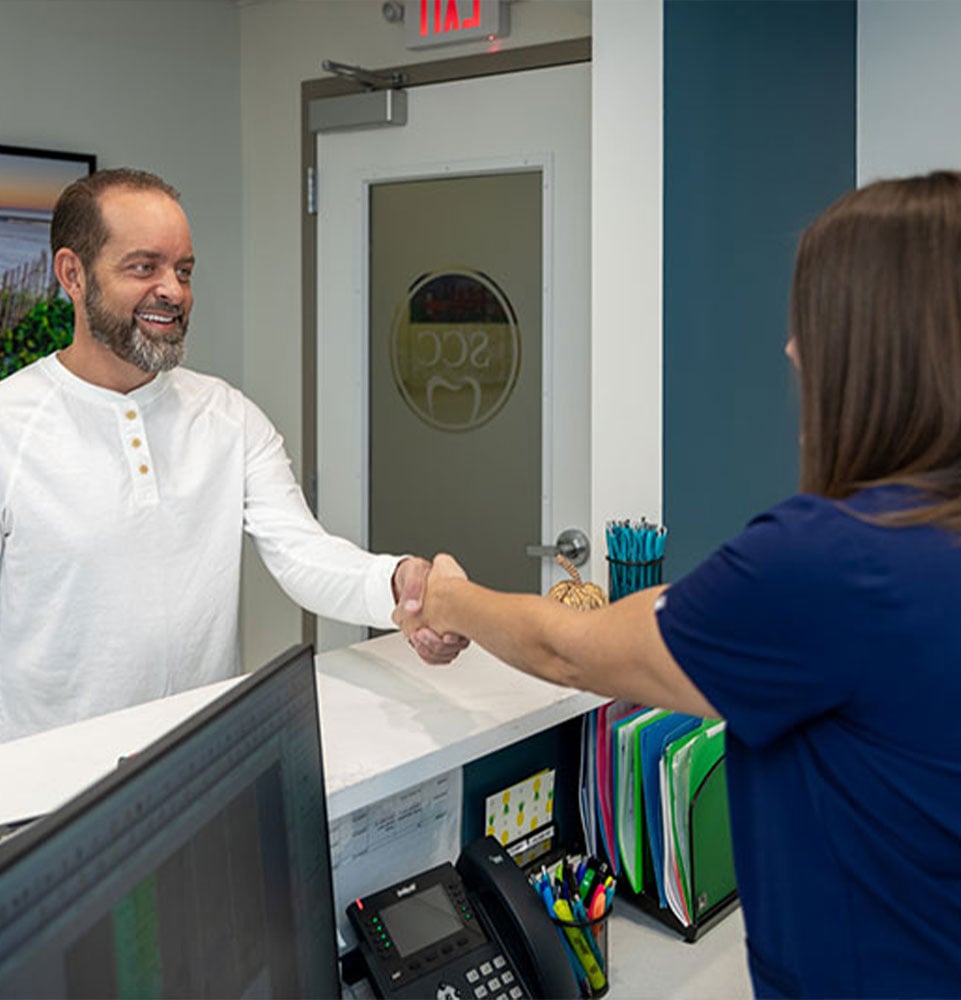 patient shaking hands with staff member at the front desk of the dental office